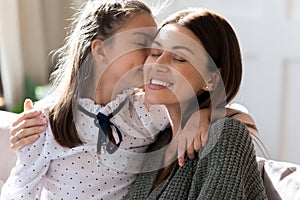 Affectionate small child girl kissing cheek of smiling loving mother.