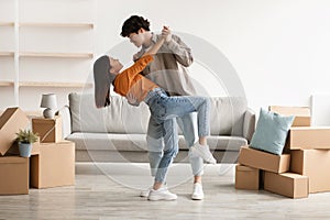 Affectionate young Asian couple dancing in their house among cardboard boxes on moving day, full length