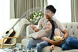 Affectionate young couple eating popcorn and watching TV on the sofa at home