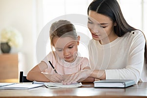 Affectionate young mother teaching small daughter reading writing.