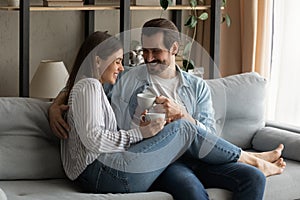 Affectionate young spouses cuddling on couch having pleasure drinking coffee