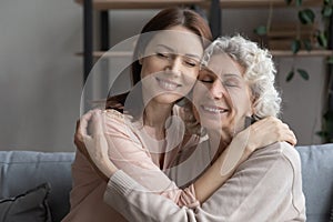 Affectionate young woman cuddling older mother at home.