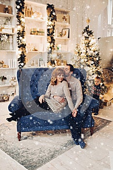 Affectionated couple on blue couch under snowflakes falling down.