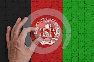 Afghanistan flag is depicted on a puzzle, which the man`s hand completes to fold