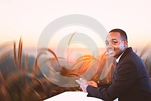 Afican businessman relaxing and using smartphone on top of mountain and sunset sky abstract background