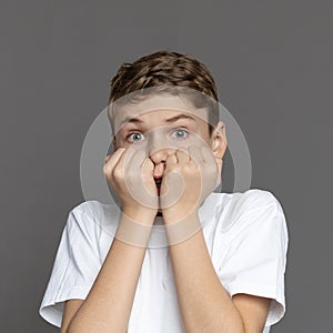 Afraid boy hiding behind hands, grey studio background