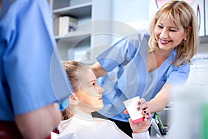 Afraid little girl is taking a glass of water from smiling dentist in dental clinic.