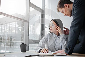 Afraid and scare young woman sit at table and look at window. Guy touch her face and hair. He wants to discriminate her. photo