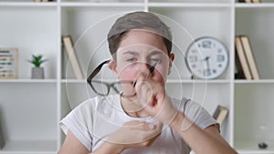 Afraid and shocked boy 13 years old in white shirt takes off glasses and cover mouth with his hand. Surprised kid