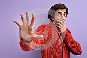 Afraid young man in defense attitude gesturing stop with hands, isolated on purple background