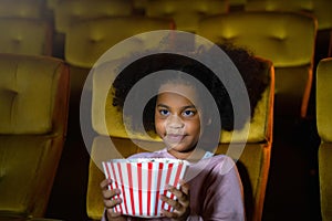 The Africa girl is seating and watching the cinema at movie theater seats. The faces have feeling happy and enjoy