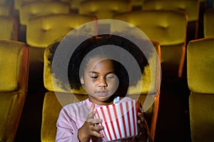 The Africa girl is seating and watching the cinema at movie theater seats. The faces have feeling happy and enjoy