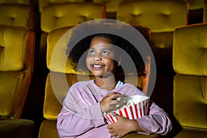 The Africa girl is seating and watching the cinema at movie theater seats. The faces have feeling happy and enjoy