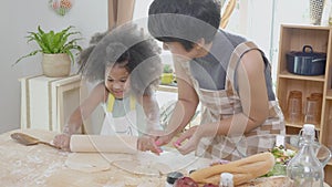 African America family with mother wearing apron rolling thresh flour for cooking with daughter together.