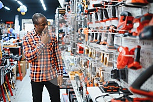 African americam man buying modern electric drill while standing in tool. Hardware construction site objects concept