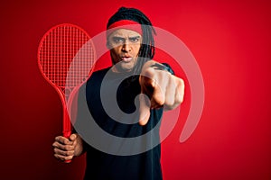 African american afro sportsman with dreadlocks holding tennis racket over red background pointing with finger to the camera and