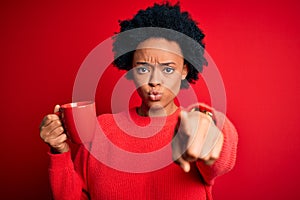 African American afro woman with curly hair drinking cup of coffee over red background pointing with finger to the camera and to