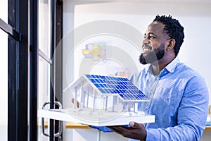 African American architect is holding house model inside working office with floor plan layout for real estate and property