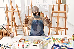African american artist man at art studio approving doing positive gesture with hand, thumbs up smiling and happy for success