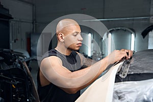 African American auto-repair shop worker preparing vehicle to repainting