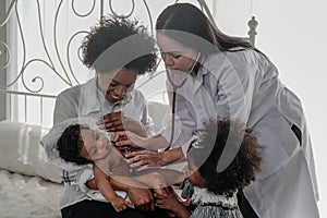 African american baby boy holding in hand of mother being examine by asian doctor with stethoscope