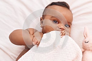 African american baby lying on bed bitting blanket at bedroom