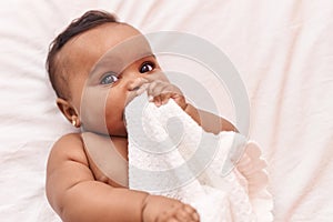 African american baby lying on bed bitting blanket at bedroom