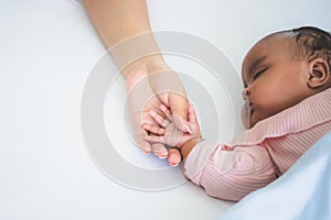African American baby newborn is 3 months old, sleeping on white bed and mother holding her hand with love