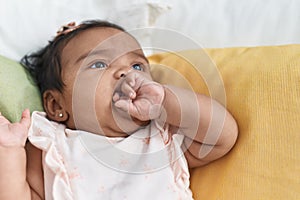 African american baby sitting on bed sucking hand at bedroom