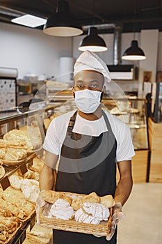 African American baker holding tray of bread in bakery