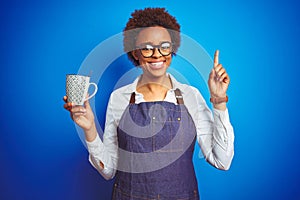 African american barista woman wearing bartender uniform holding cup over blue background surprised with an idea or question