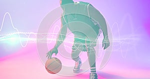 African american basketball player dribbling ball by illuminated wave patterned lines