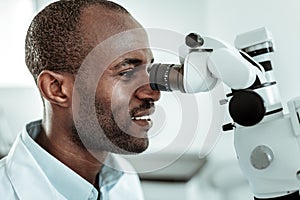 African American beaming stomatologist actively working with microscope