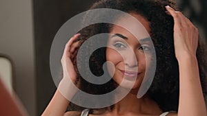 African American beautiful woman beauty routine in bathroom girl looking mirror reflection touching curly hair healthy