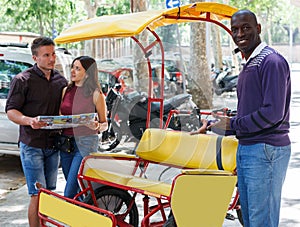 African-American bikecab driver offering rickshaw service to couple photo