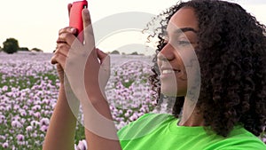 African American biracial girl teenager female young woman in a field of pink poppy flowers taking photographs on her smart phon