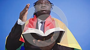 African american black man with elegant suit rainbow flag covering his shoulders holding holy bible in the hands. Gay