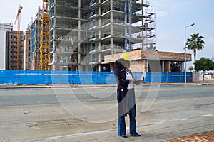 African-American black woman construction manager in yellow hardhat set out to check the construction of the flats. She is holding