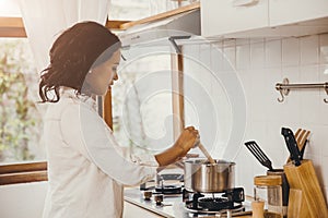 African American Black woman cooking boiling soup in the kitchen at home