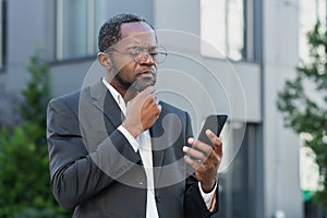 African american boss outside office building with phone in hands reading bad news online, man received notification