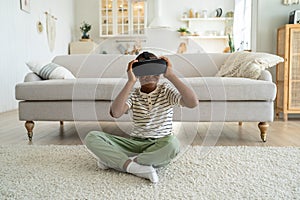 African American boy child sitting on floor at home using virtual reality device watching 3d video