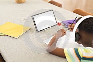 African American boy focuses on homework, tablet with blank screen nearby with copy space