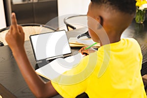African American boy focusing on writing at home with copy space, tablet with blank screen nearby