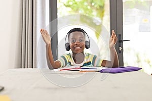 African American boy with headphones gestures during an online class