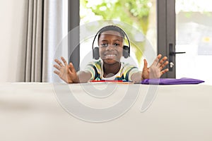 African American boy with headphones smiles at the camera, hands outstretched, with copy space