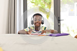 African American boy with headphones smiles while studying at home in an online class