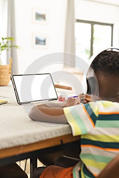 African American boy with headphones uses a tablet with a blank screen at a table with copy space