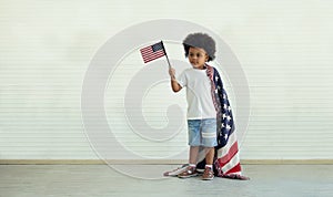 An African American boy holding little usa flags standing with us blanket on his shoulder