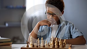 African American boy logically thinking out strategy of playing chess, hobby