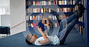 African-American boy lying on floor and reading book in modern school library